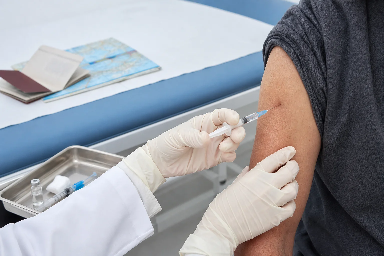 Travel health nurse in a bright Scottsdale clinic administering a vaccine to an international traveler, vaccination records and passport on the desk, globe visible in the background, warm clinical lighting