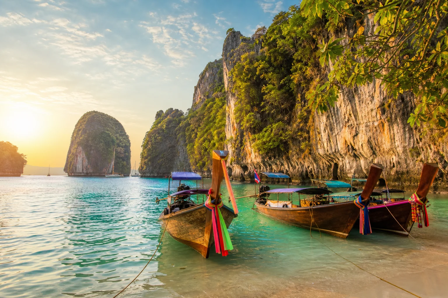 Thailand travel vaccines guide: traditional longtail boats anchored beside limestone cliffs at a Thailand island bay